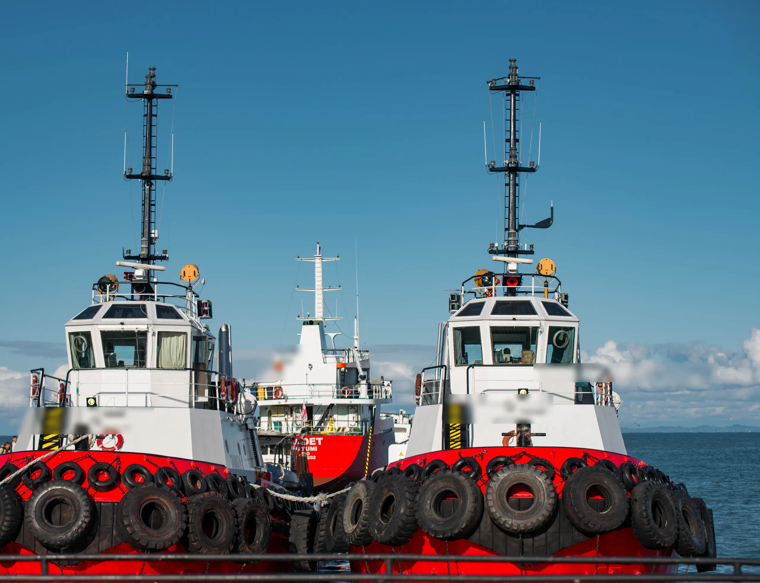 Two harbor tugboats at a working dock under a clear sky